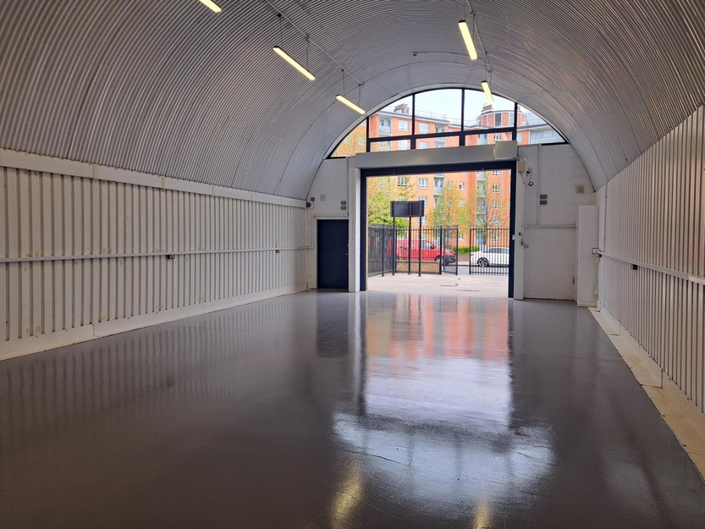 The front of an arch, with high level glazing, an open electric roller shutter entrance big enough for vehicle access, and a pedestrian door.