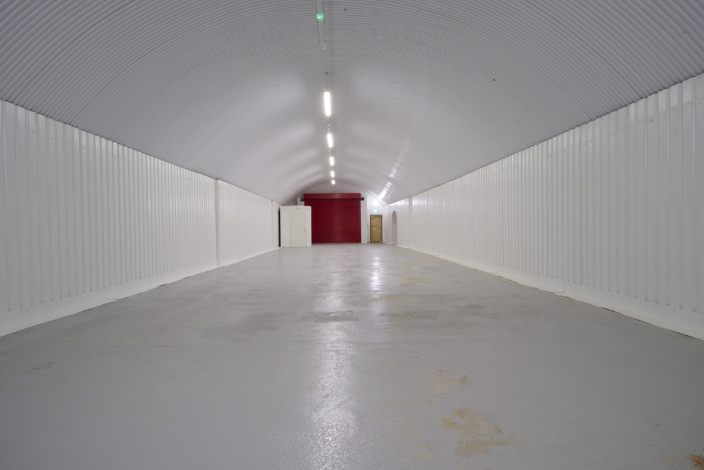 An empty arch with white lining, facing the front electric roller shutter entrance, which is closed. There is a WC cubicle at the front of the arch.