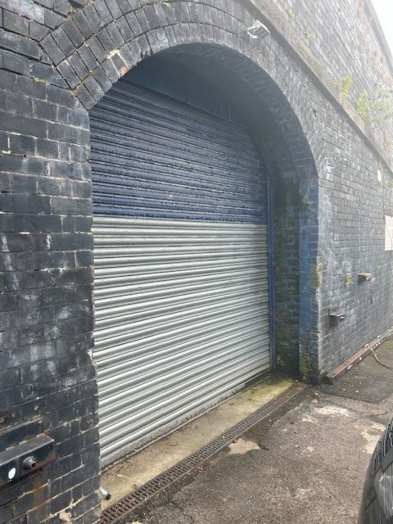 The front of an arch with a closed electric roller shutter entrance big enough for vehicle access. 