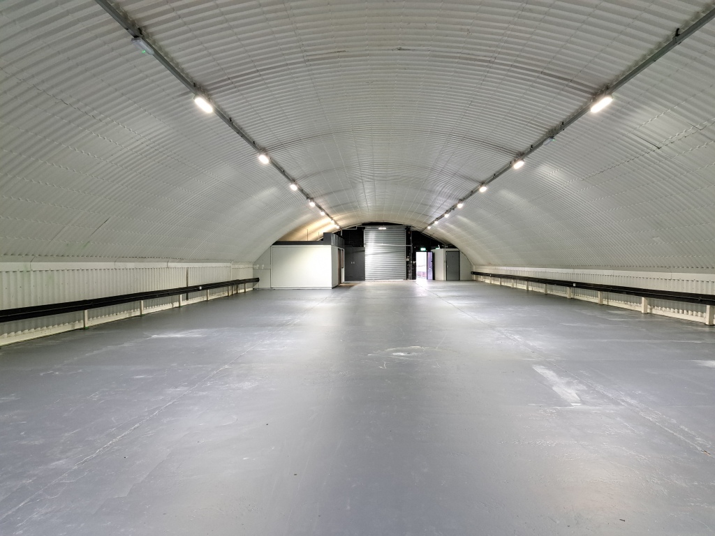 An empty arch with white lining, facing the front electric roller shutter entrance, which is closed. There is a WC cubicle at the front of the arch.