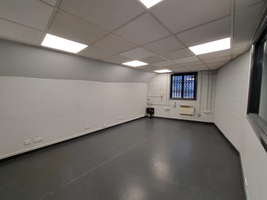 An empty arch with white lining, facing the front electric roller shutter entrance, which is closed.