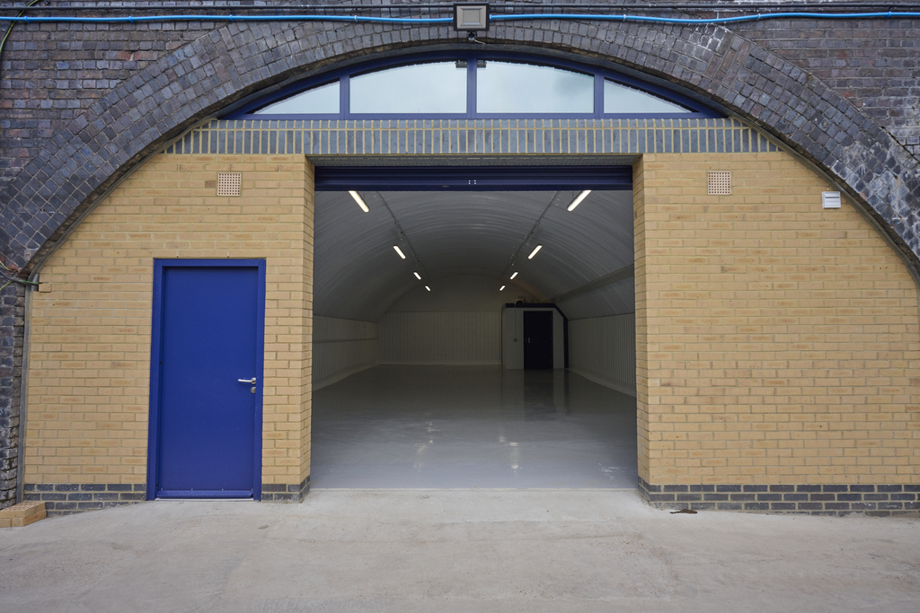The front of an arch, with high level glazing, an open electric roller shutter entrance big enough for vehicle access, and a pedestrian door.
