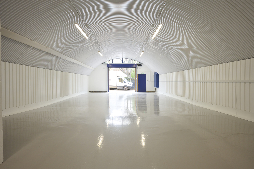 An empty arch with white lining, facing the front electric roller shutter entrance, which is open.