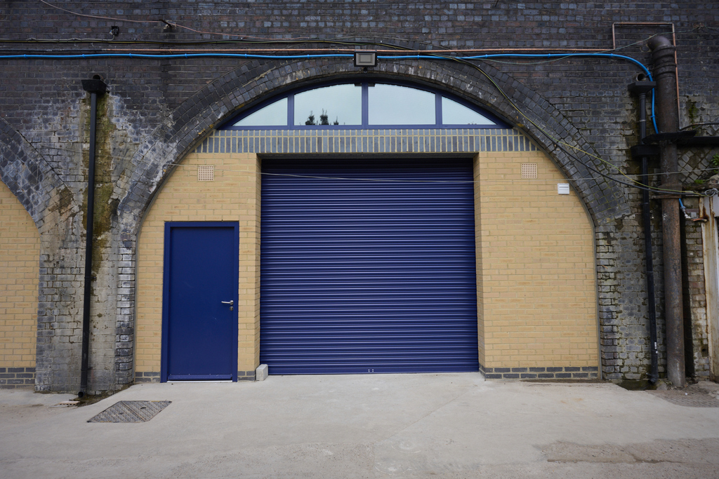 The front of an arch, with high level glazing, a closed electric roller shutter entrance big enough for vehicle access, and a pedestrian door.