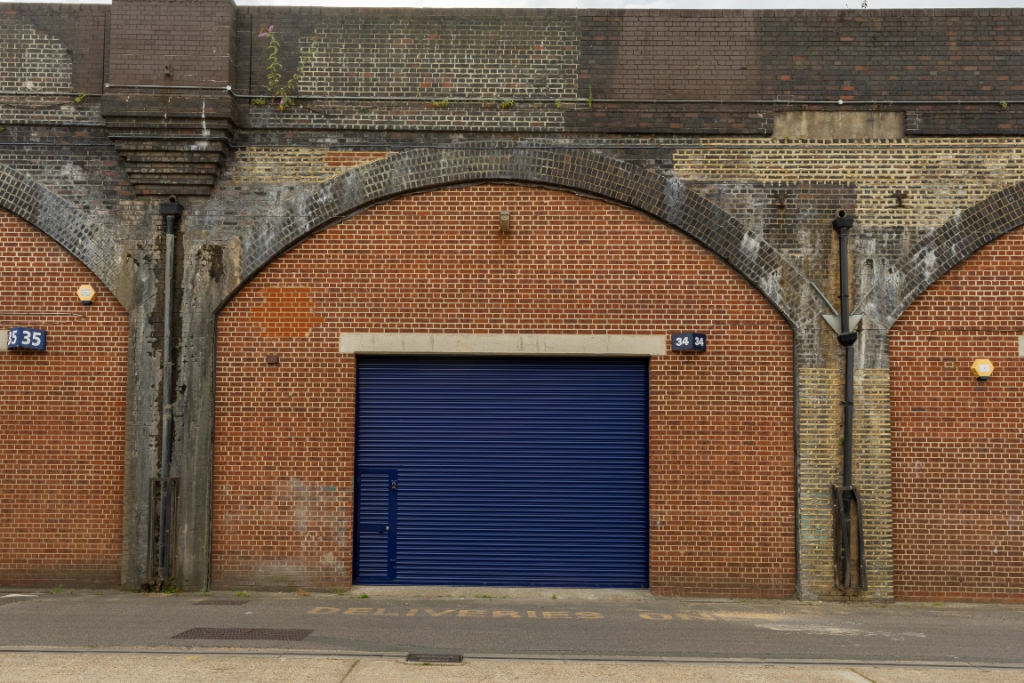 The front of an arch with a closed electric roller shutter entrance big enough for vehicle access.