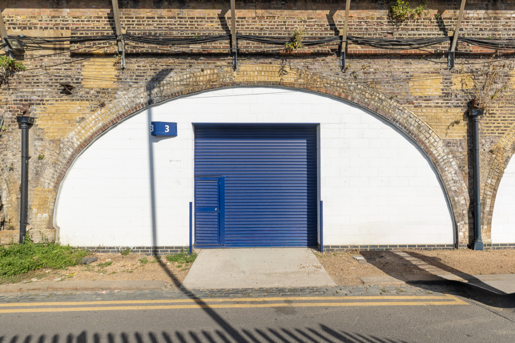 The front of an arch with a closed electric roller shutter entrance big enough for vehicle access.