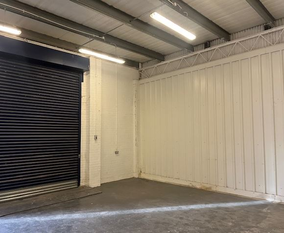 The interior of a warehouse unit, facing the front electric roller shutter, which is closed and large enough for vehicle access.