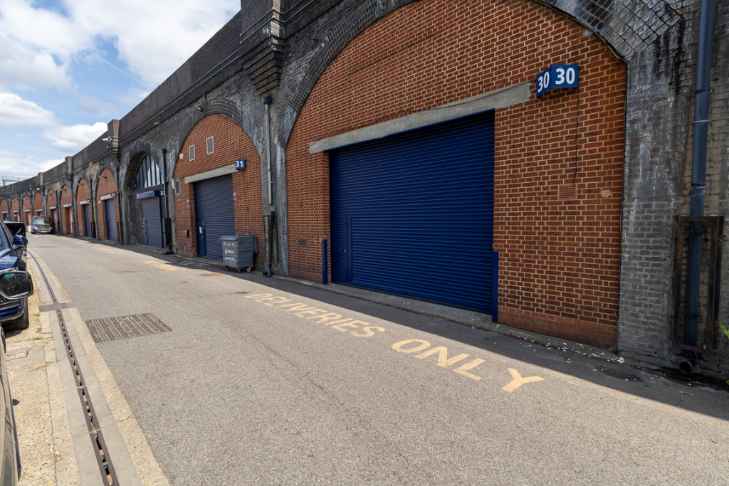 The front of an arch with a closed electric roller shutter entrance big enough for vehicle access, and separate pedestrian door.

