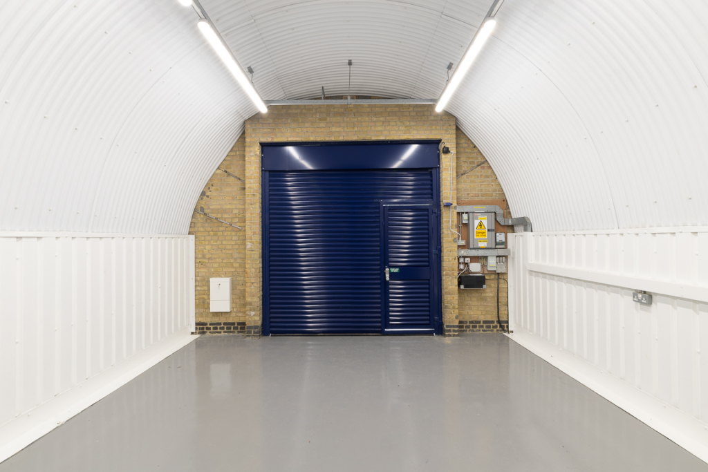 An empty arch with white lining, facing the front electric roller shutter entrance, which is closed.