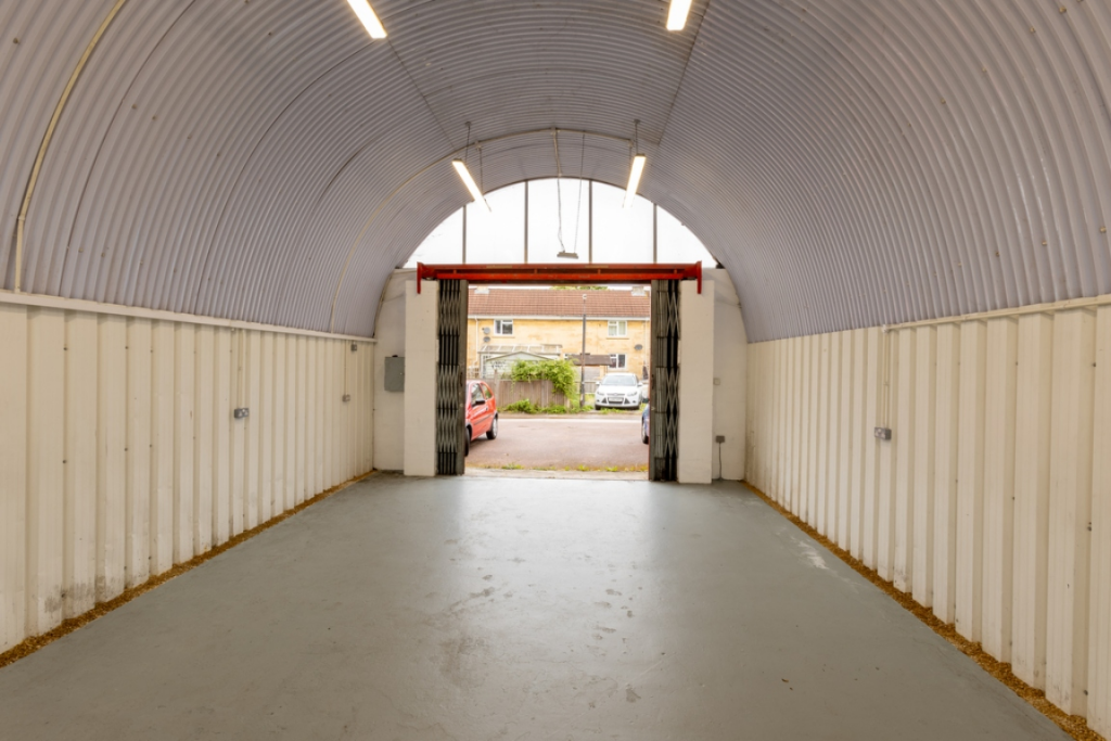 An empty arch with white lining, facing the front electric roller shutter entrance, which is open.
