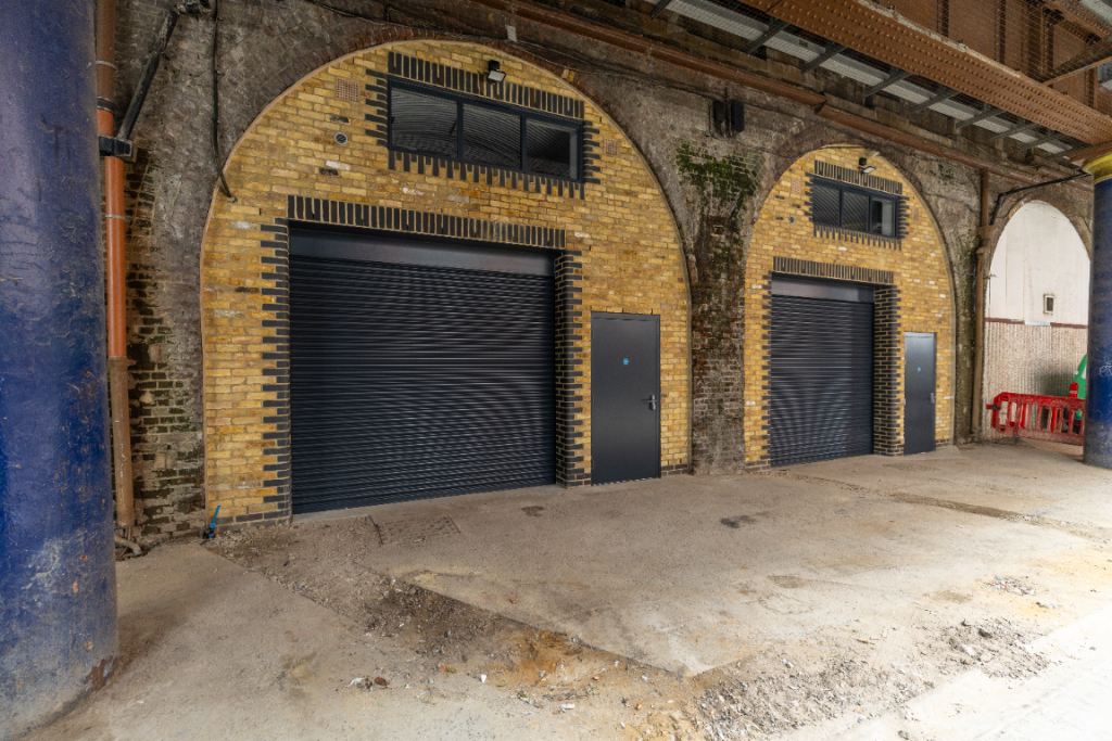 The front of an arch with a closed electric roller shutter entrance big enough for vehicle access, and separate pedestrian door.