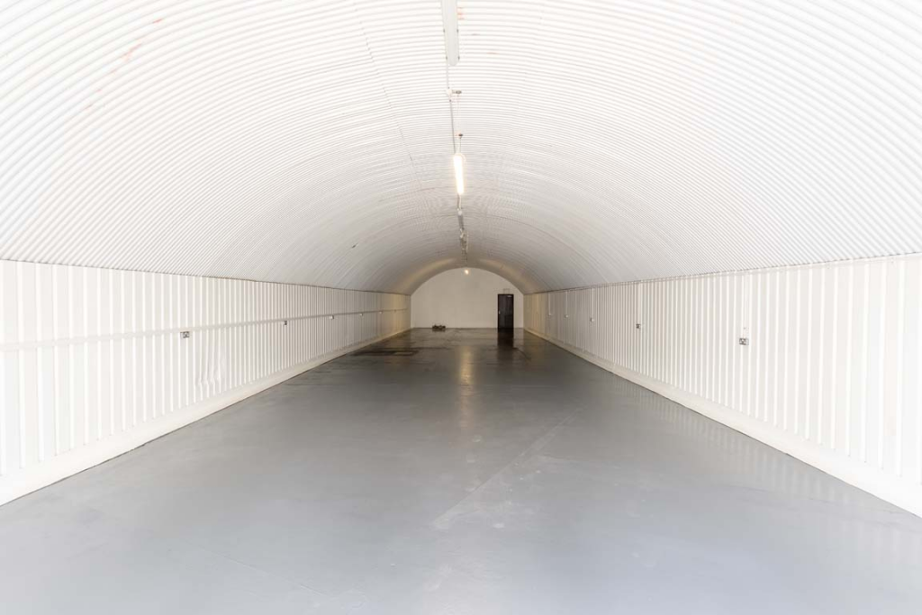 An empty arch with white lining, facing the front electric roller shutter entrance, which is open.