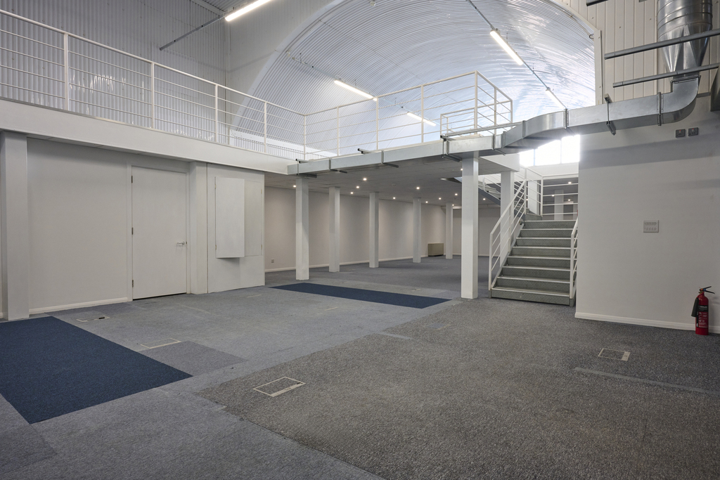 An arch with white lining and a ground floor level and a mezzanine level, connected by stairs.