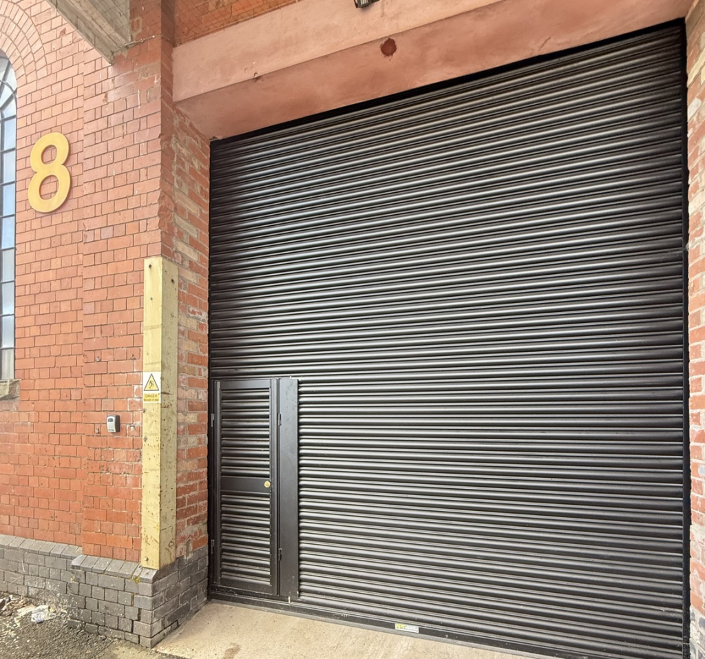 The interior of a warehouse unit, facing the front electric roller shutter, which is closed and large enough for vehicle access.