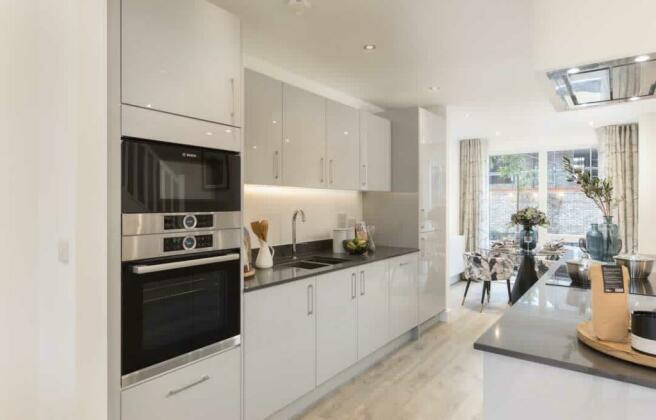 A cream and grey kitchen with dark quartz woodtops, double oven and central island. Dining table in