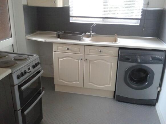 A compact kitchen featuring cream cabinetry, a ...