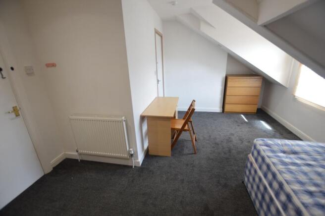 A cozy single bedroom featuring a slanted ceili...