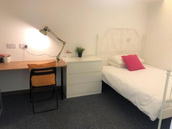 A neat and cozy single bedroom featuring a whit...