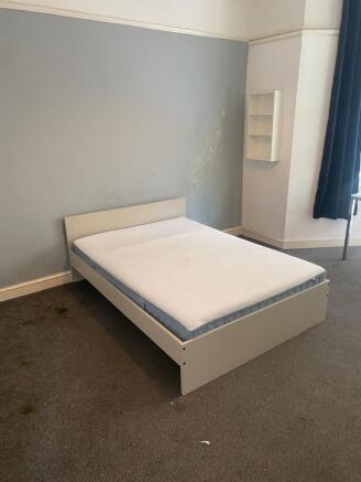 A plain bedroom featuring a single bed frame wi...