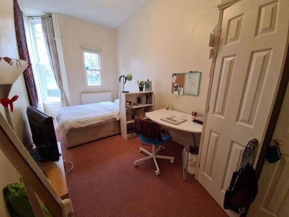 A tidy bedroom featuring a single bed, a desk w...