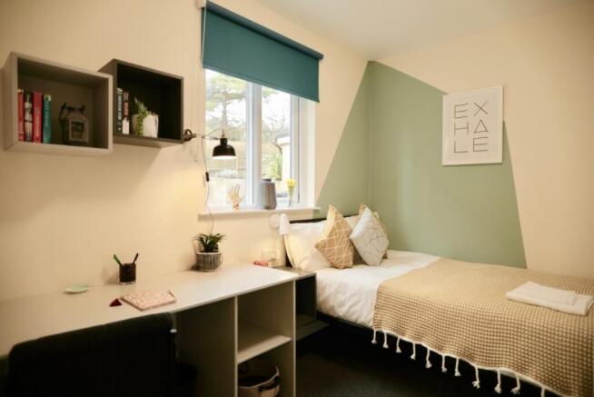 A cozy single bedroom featuring a window with a...