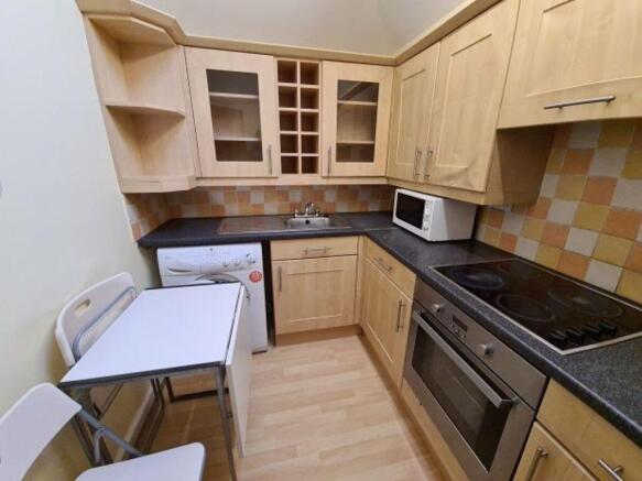Compact fitted kitchen with light wood cabinets...