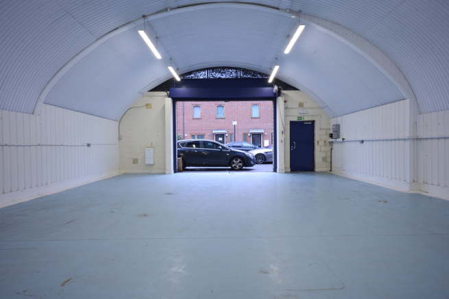 An empty arch with white lining, facing the front electric roller shutter entrance, which is open.