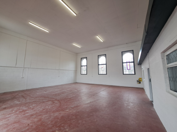 The interior of a warehouse unit, facing the front electric roller shutter, which is closed and large enough for vehicle access.