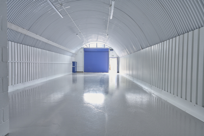 An empty arch with white lining, facing the front electric roller shutter entrance, which is closed.