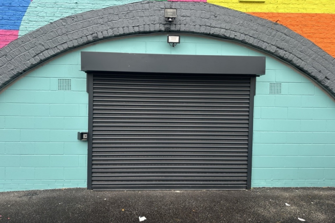 The front of an arch, with high level glazing, a closed electric roller shutter entrance big enough for vehicle access, and a pedestrian door.