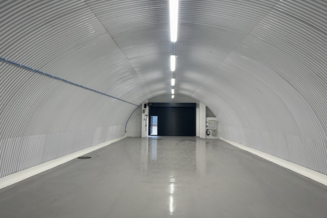 An empty arch with white lining, facing the front electric roller shutter entrance, which is closed.