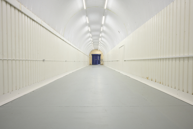 An empty arch with white lining, facing the front electric roller shutter entrance, which is closed.