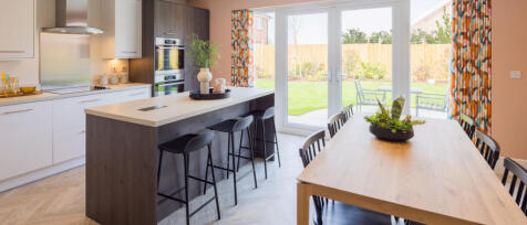 Modern kitchen and dining area with large glass doors opening to a garden, featuring white cabinetry