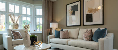 Living room with beige sofa, abstract artwork, large bay window with brown curtains, and decorative