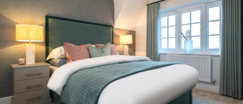 A cosy bedroom with a large bed, pastel pillows, and soft lighting, overlooking a window with curtai