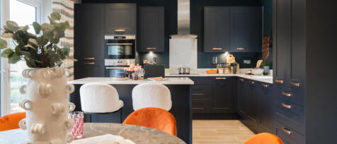 Modern kitchen with dark navy cabinets, white marble worktops, a central island, and cosy orange and