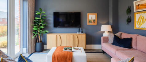 Modern living room with a pink sofa, wall-mounted TV, framed artwork, plants, and a glass door leadi