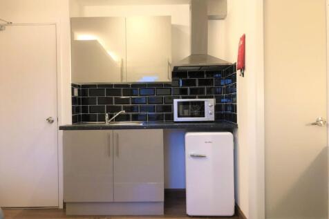 A modern compact kitchen featuring glossy cabin...