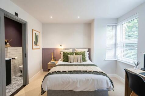 A bright, modern master bedroom featuring a com...
