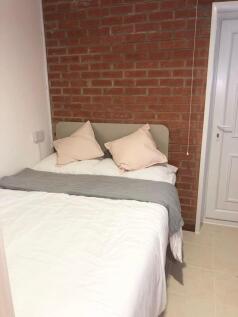 Bright, neatly made bedroom with exposed brick ...