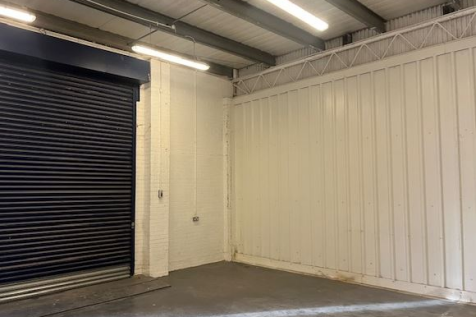 The interior of a warehouse unit, facing the front electric roller shutter, which is closed and large enough for vehicle access.