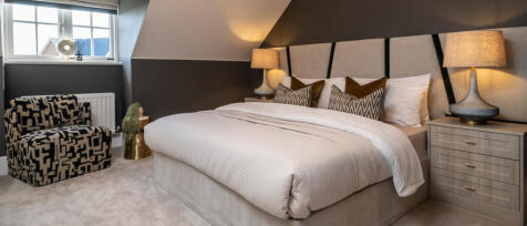 A contemporary bedroom with a beige bed, patterned cushions, bedside lamps, a window, and a black an