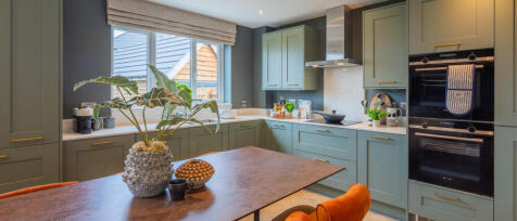 Modern kitchen with green cabinets, a wooden dining table, and a window with a view of neighbouring