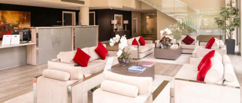 Modern hotel or residential building lobby with cream sofas, red cushions, glass staircase, and deco