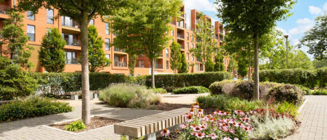 Modern residential building with brick facades surrounded by green trees, shrubs, and flowering plan
