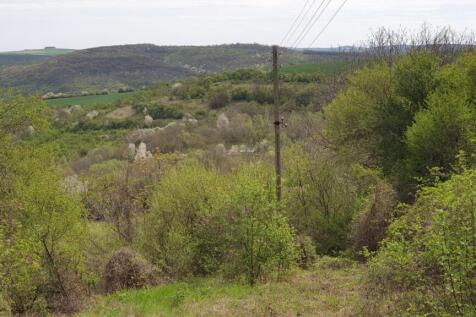 Landscape of a green valley featuring trees and scattered houses under a cloudy sky.