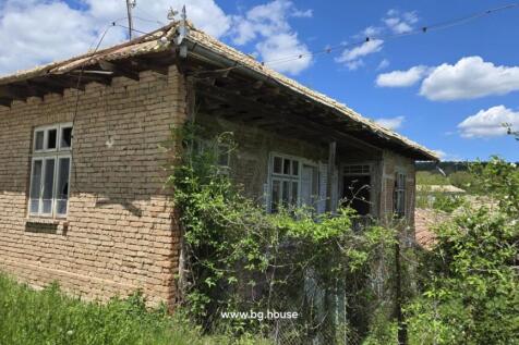 Old brick house with tiled roof and white framed windows surrounded by greenery in Osikovo village
