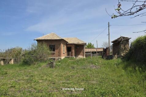 View of the Bulgarian house from the garden area showing grass, trees, and outbuilding