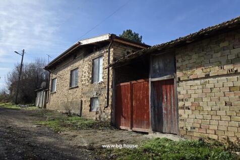 Exterior view of a brick house with a red wooden gate and two dogs on the dirt road beside it.