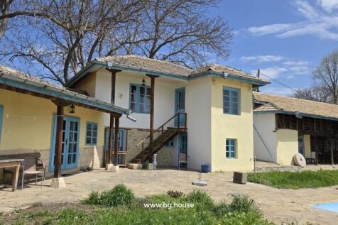 Traditional Bulgarian rural house with stone roof and blue window frames surrounded by trees